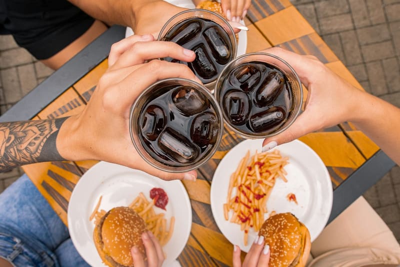 four glasses of cola raised over burgers