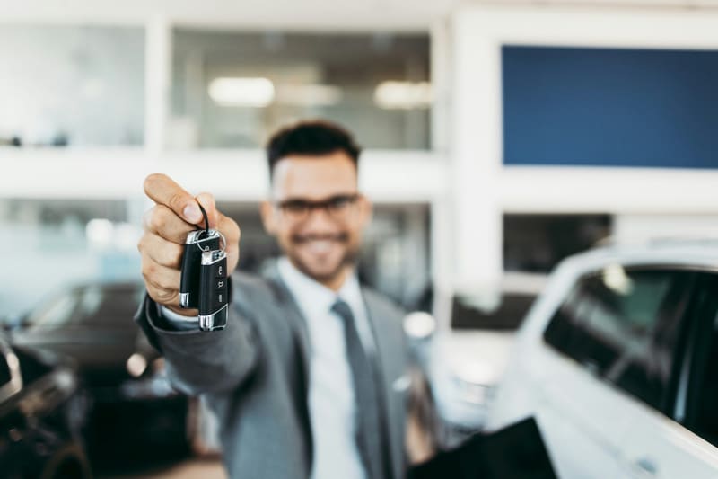 a salesman holding out a car key