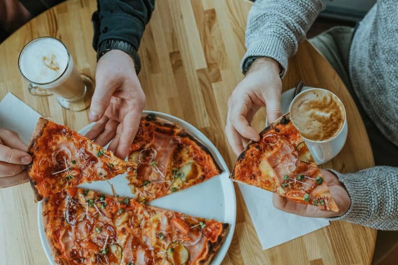 two people taking slices of pizza