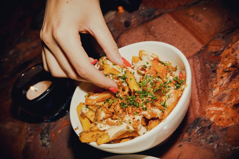 a hand taking loaded fries from a bowl