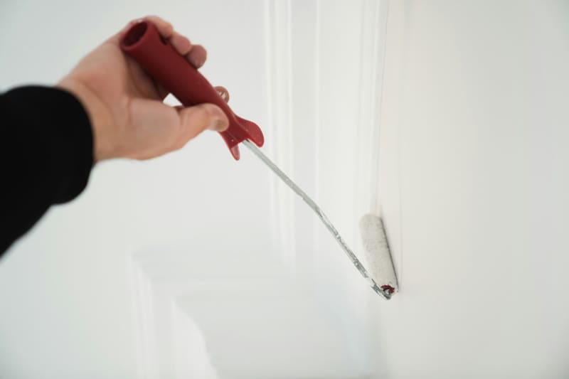 a hand rolling white paint on a wall