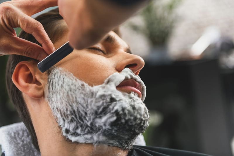 a barber shaving a lathered beard