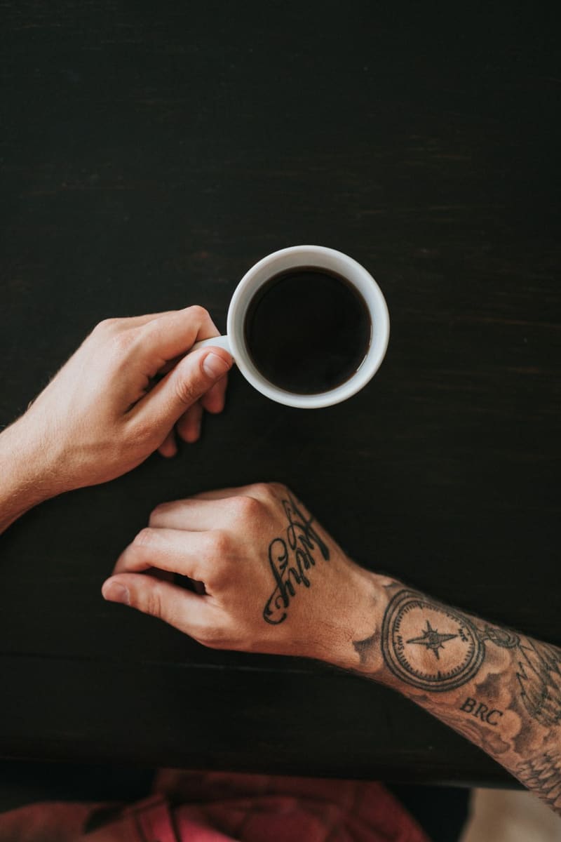 a tattooed hand holding an espresso