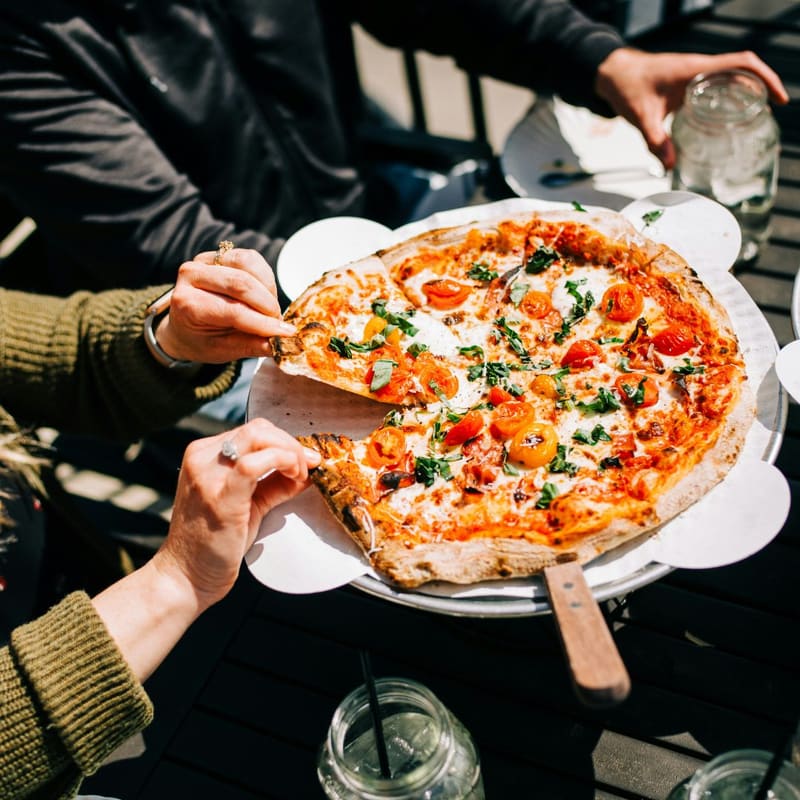 hands serving pizza at a table
