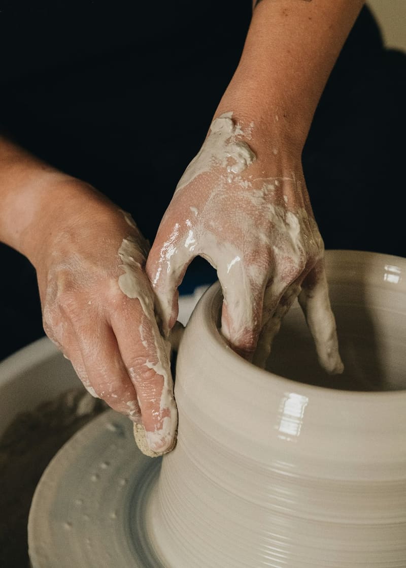 clay hands shaping a pot on a wheel