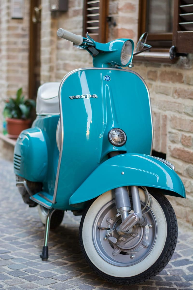 a turquoise vespa against brick