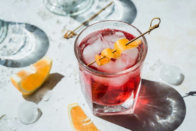a red cocktail on ice with fruit