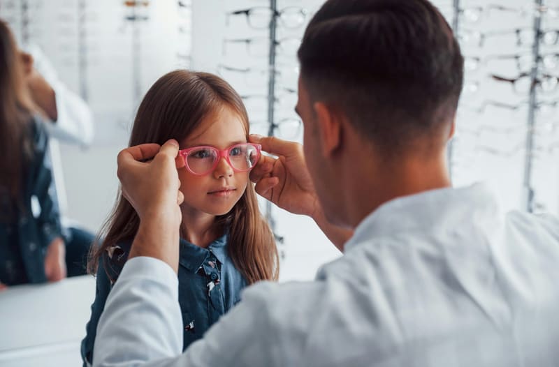 an optician fitting a child with glasses