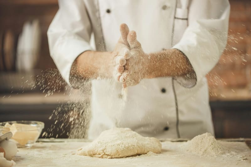 a baker dusting flour over dough